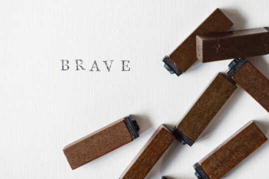The word BRAVE typed onto white paper, showing loose keys